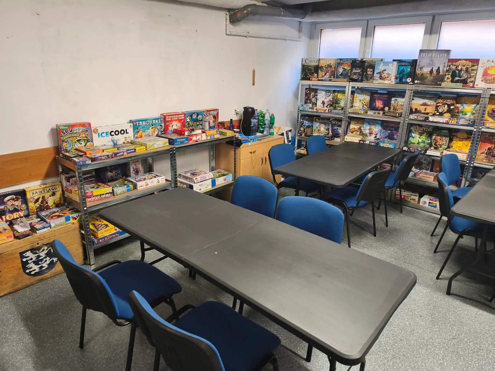 Sala klubowa Dąbrowskiego Klubu Gier z dużymi stołami do gry oraz regałami pełnymi planszówek.
